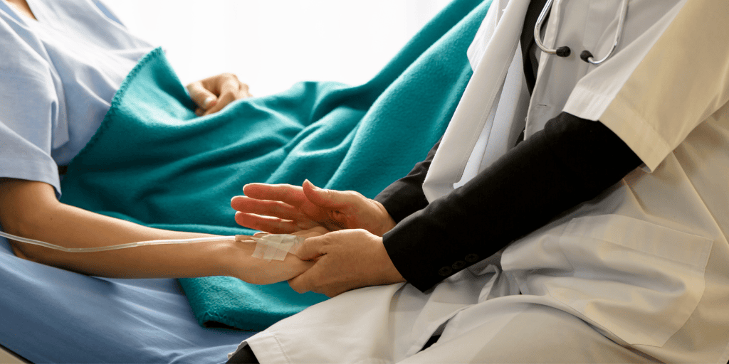 Doctor comforts a woman in a hospital bed, patting her hand
